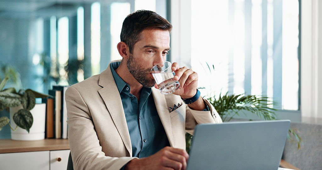 Personnage masculin buvant un verre d'eau sur son lieu de travail devant son ordinateur portable